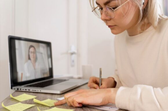 Studentessa che cerca di mantenere la sua concentrazione mentre segue una lezione online da casa con cuffie e computer portatile