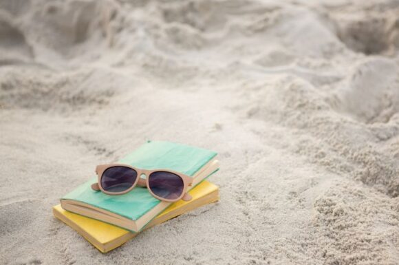 Occhiali da sole su due libri e la sabbia. La crescita personale non va in vacanza